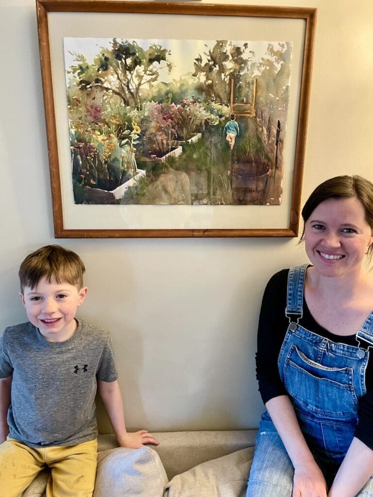 Mother and son sit next to their commissioned watercolor painting of a garden
