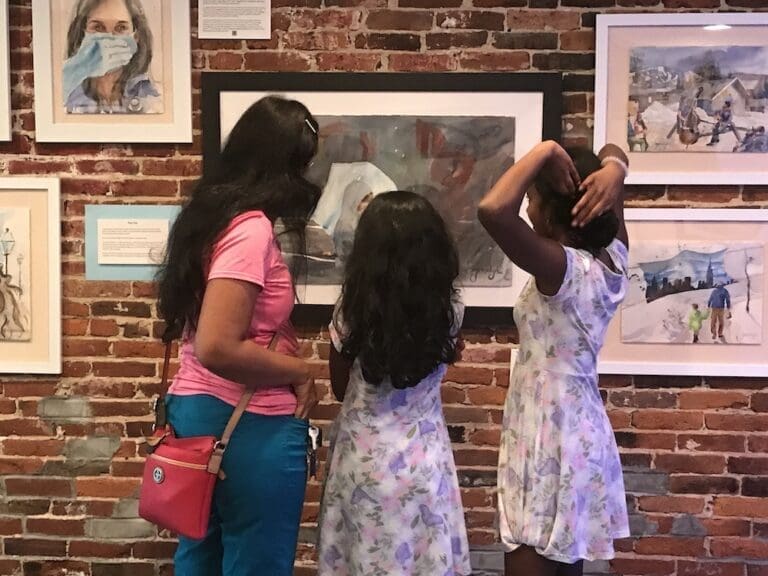 A mother and her daughters crowd around a painting of the COVID years to study it.