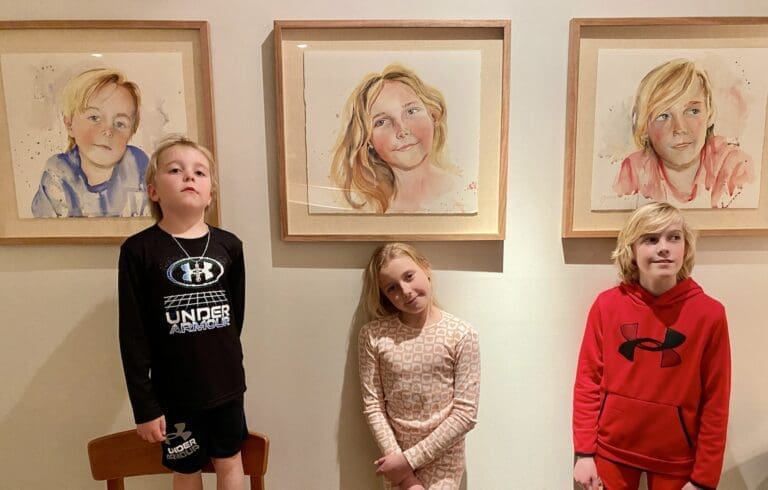 Three children pose next to their watercolor portraits, recreating their expressions from the painting.