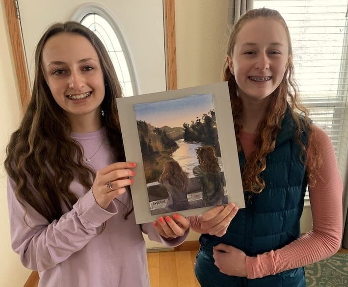 Two girls holding watercolor of two girls looking at the Yampa River.