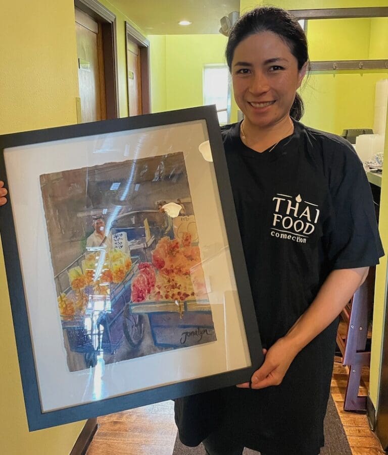 Woman holding watercolor painting of food vendors selling fruit.